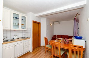 Cocina compacta con armarios blancos, encimera de madera y zona de comedor con mesa y sillas.