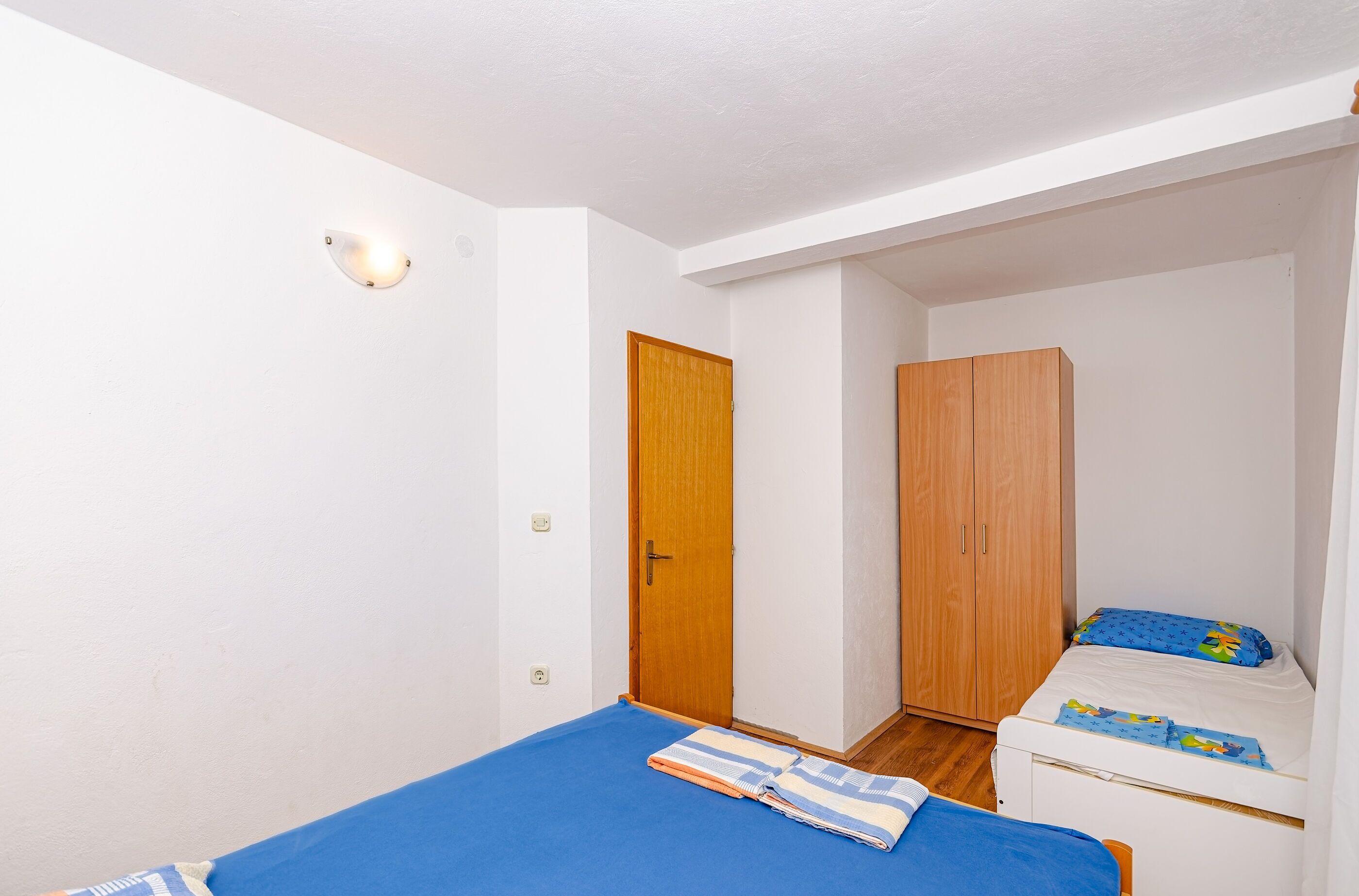 A small, well-lit bedroom with a single bed, a wooden wardrobe, and a closet.