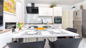 A modern kitchen with white cabinets, a stainless steel refrigerator, and a dining table set for four. - Apartment Lada (Supetar)