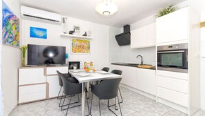 A modern kitchen with white cabinets, a dining table with chairs, a TV, and a microwave. - Apartment Lada (Supetar)
