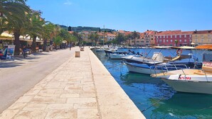 A marina with boats docked, a stone-paved walkway, and buildings with red roofs in the background. - Apartment Lada (Supetar)