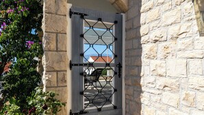 A stone wall with a metal gate and a view of a red-roofed building through a window. - Apartment Pepica (Postira)