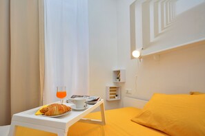 A hotel room with a bed, a bedside table with a croissant, a cup of coffee, and a glass of orange juice. - Apartment Pepica (Postira)