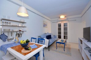 A compact living space with a dining table, blue chairs, a sofa, and a TV. - Apartment Pepica (Postira)