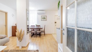 Una sala de estar moderna con comedor, piso de madera, sofá blanco, mesa de centro, un florero con plumas de pampa y un ventanal con vidrio esmerilado.
