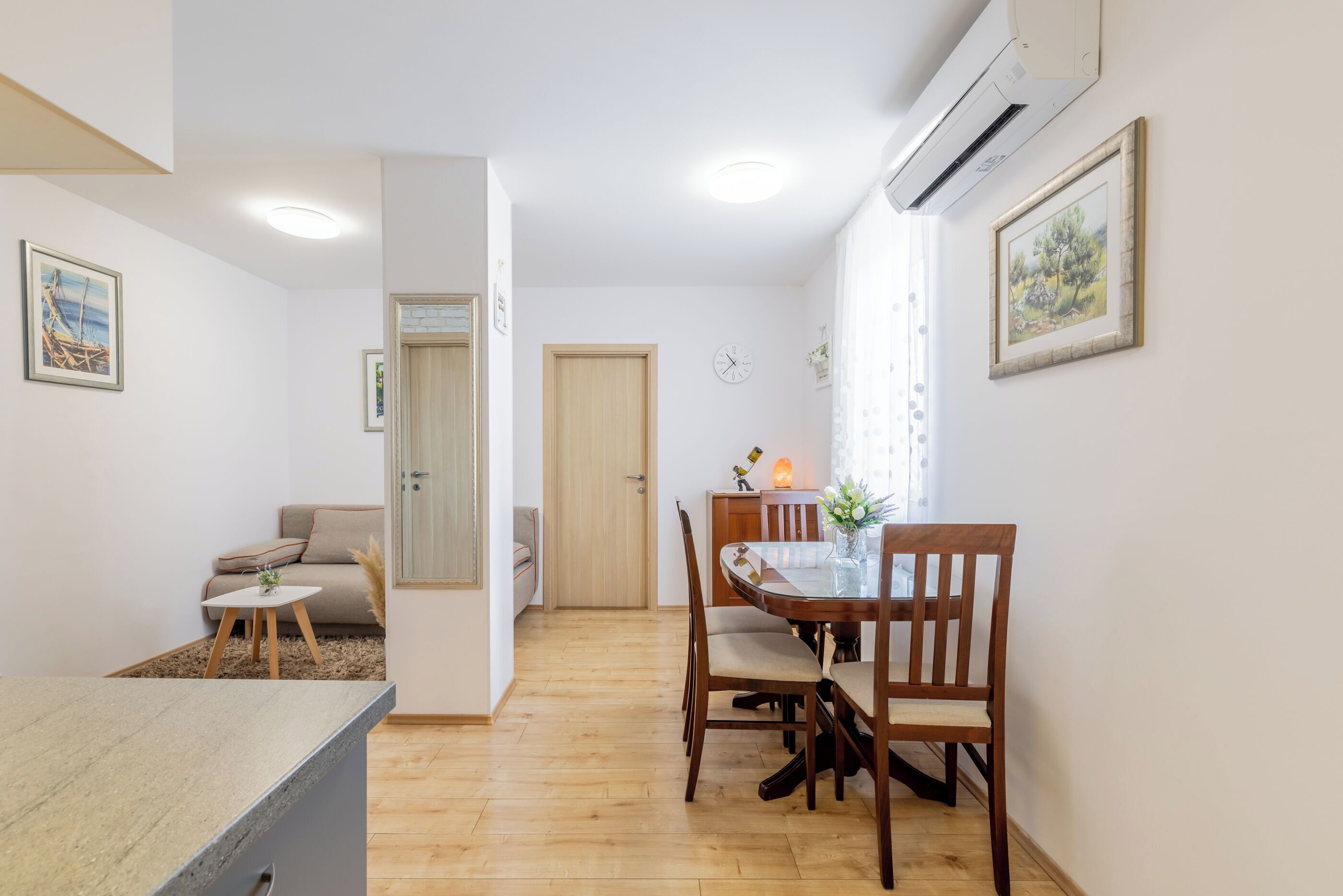 A modern living room with a dining area, wooden flooring, and a large window with curtains.