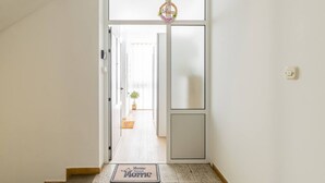 Un pasillo con un felpudo que dice 'Welcome Home', una puerta con un cartel de 'Welcome' y una planta a lo lejos.