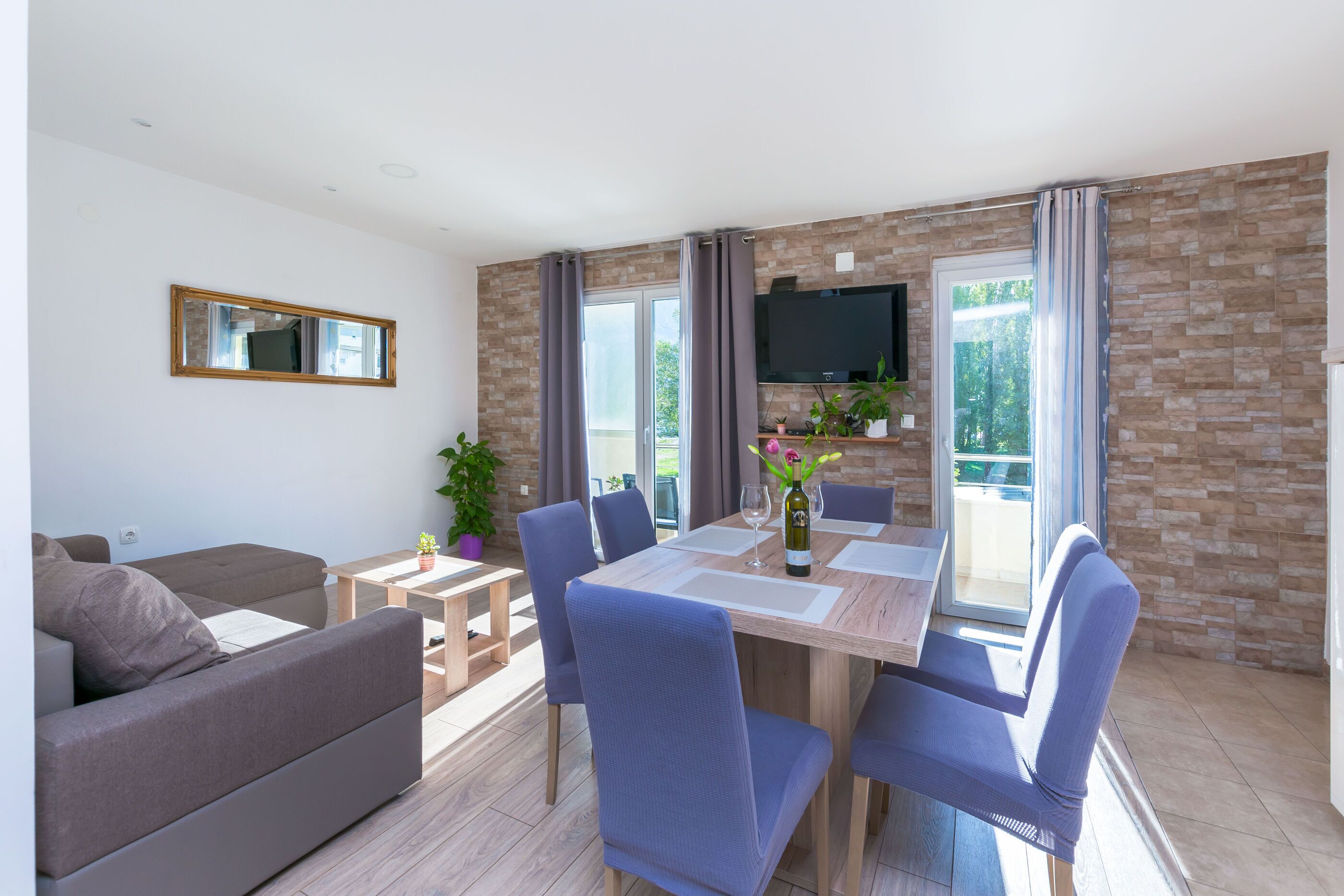 Ein modernes Wohnzimmer mit einer Couch, einem Esstisch mit Stühlen, einem an der Wand befestigten Fernseher und einem Balkon mit Blick.