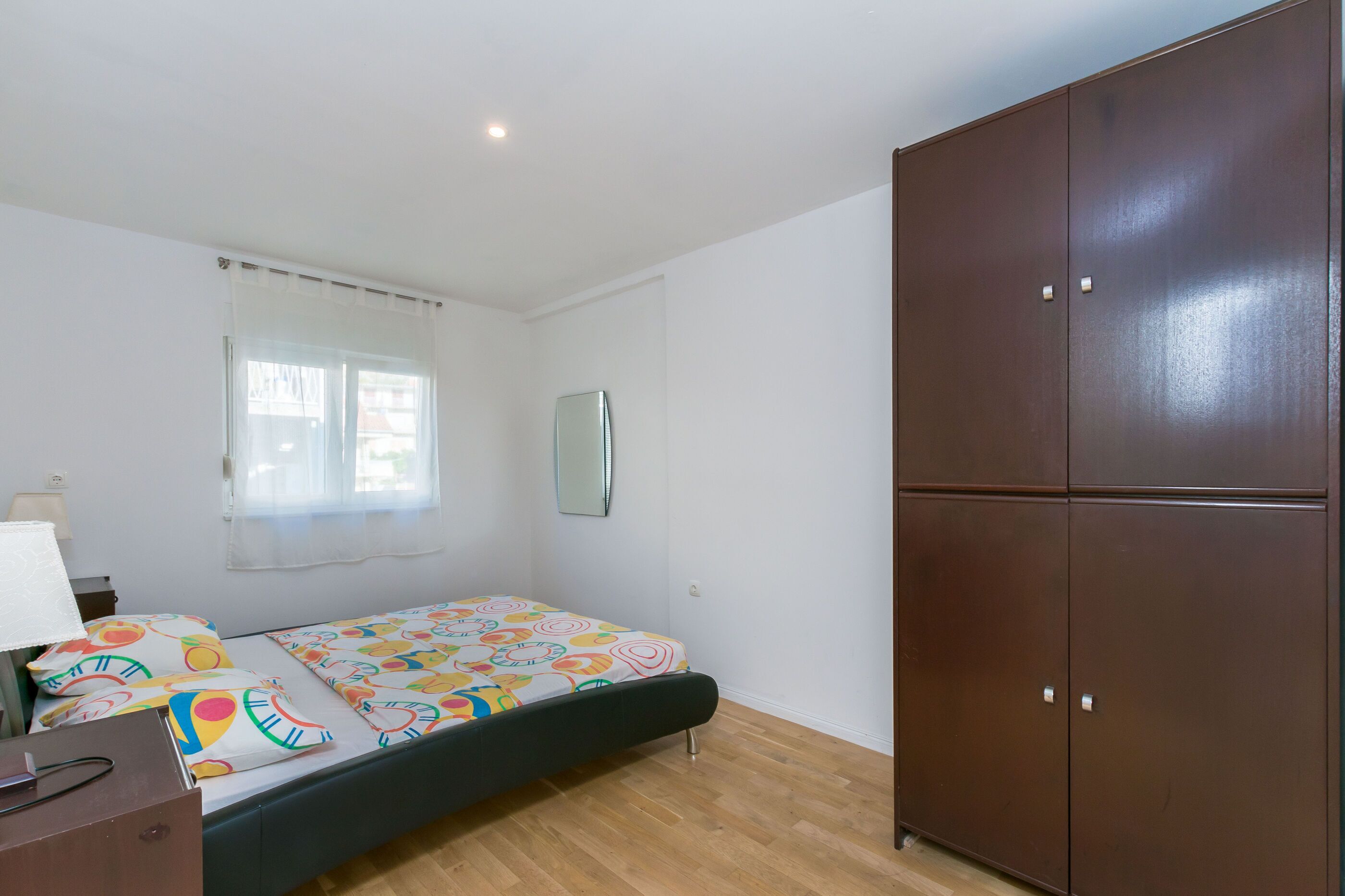 A bedroom with a bed, a wardrobe, a mirror, and a window with curtains.