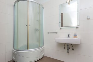 A modern bathroom with a glass-enclosed shower, a white sink, and a mirror above it. - Apartment Ivana (Omis)