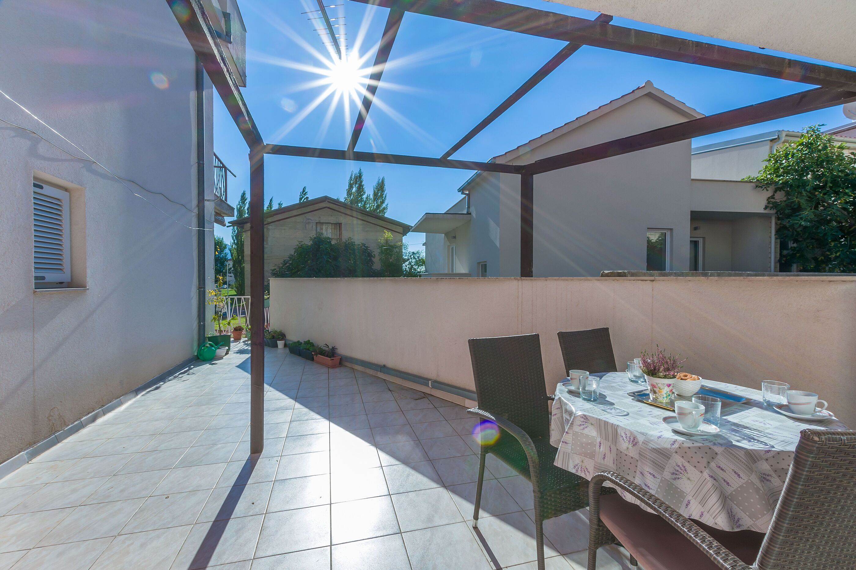 A covered patio with a table set for dining, surrounded by chairs, and a view of neighboring houses.
