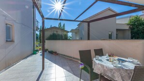 A covered patio with a table set for dining, surrounded by chairs, and a view of neighboring houses. - Apartment Ivana (Omis)