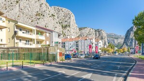 A street with buildings, a road, and a mountain in the background. - Apartment Ivana (Omis)