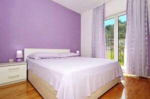 A bedroom with a bed, a nightstand, and a window with curtains. - Apartments Nedjeljko (Arbanija)