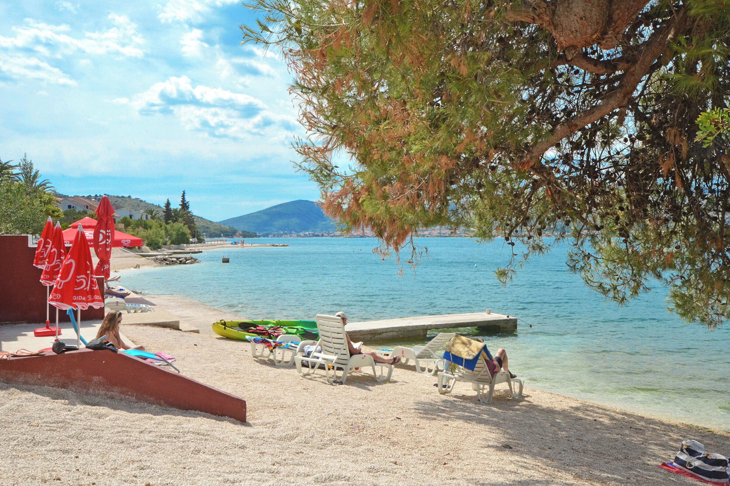 Une plage aux eaux cristallines, quelques bateaux et un arbre qui offre de l’ombre.