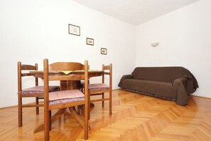 Egy szoba, melyben egy fa étkezőasztal, négy szék és egy barna kanapé található.