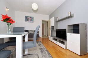 Ein modernes Wohnzimmer mit Glastisch, grauen Sesseln, einer Couch, einem Flachbildfernseher und einem weißen Schrank.