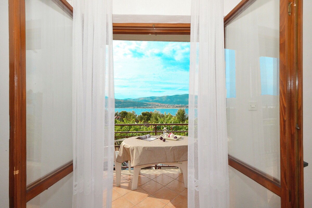 A balcony with a table set for two, overlooking a scenic landscape with hills and a body of water.