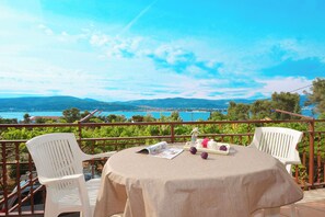 A round table with a beige tablecloth, two white chairs, and a view of a coastal landscape with mountains and a body of water. - Apartments Nedjeljko (Arbanija)