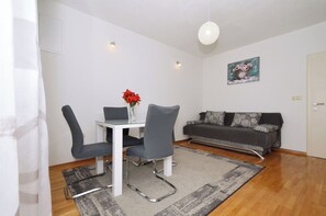 A modern living room with a dining table, two chairs, a grey sofa, a grey rug, and a painting on the wall.