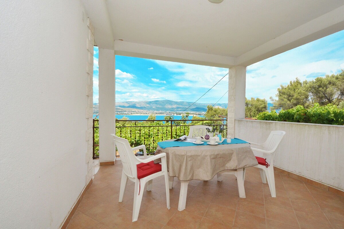 A balcony with a table and chairs, overlooking a scenic landscape with mountains and a body of water.