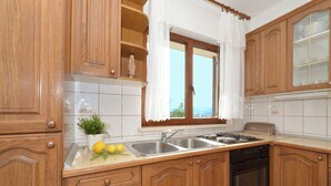 Une cuisine avec des meubles de rangement en bois, un évier à deux bacs, une cuisinière et une fenêtre avec des rideaux.
