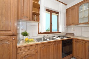 A kitchen with wooden cabinets, a double sink, a stove, and a window with curtains.