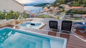 A pool area with a hot tub and lounge chairs overlooking a coastal town. - Apartment Vila Grscica (Blato)