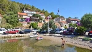 A waterfront area with parked cars, a small boat, and a person in swimwear. - Apartment Vila Grscica (Blato)