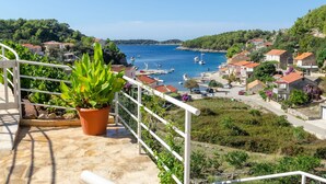 A balcony with a potted plant, overlooking a coastal town with boats, houses, and greenery. - Apartment Vila Grscica (Blato)