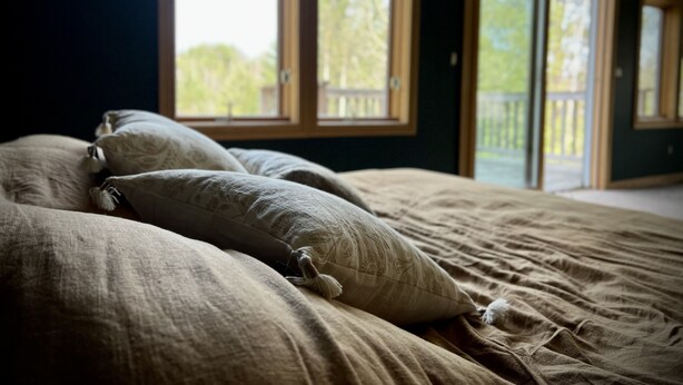 Une chambre à coucher avec un grand lit, de nombreux oreillers et une vue sur un balcon par la fenêtre.