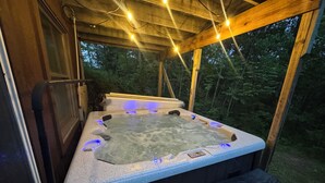 Un bain à remous doté d’un système d’éclairage intégré, entouré d’une terrasse en bois et protégé par une paroi en verre.