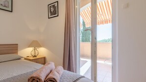 Une chambre d’hôtel avec un lit, une table de chevet avec une lampe, une fenêtre avec des rideaux et une vue sur le balcon extérieur.