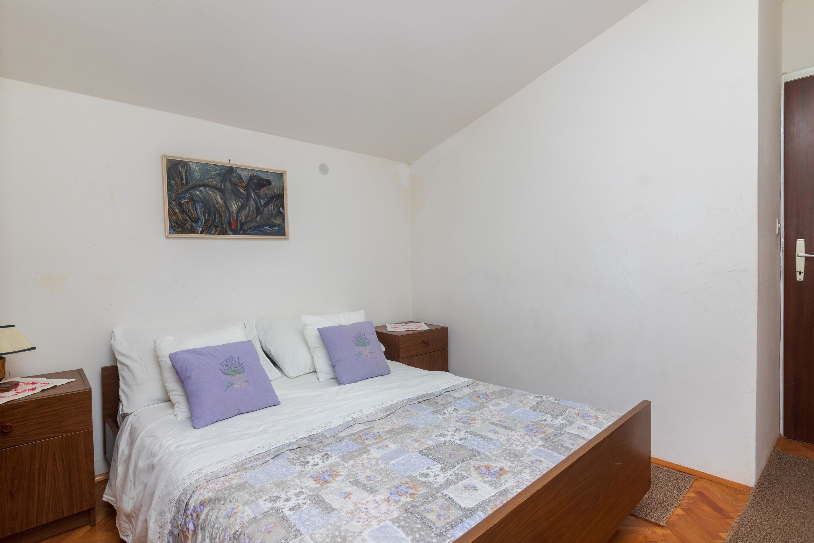 Une chambre à coucher avec un lit, des tables de chevet, un tableau au mur et une porte.