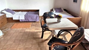Una habitación acogedora con dos camas, una mesa de comedor y una silla. Hay una alfombra pequeña en el suelo y una lámpara fijada a la pared.