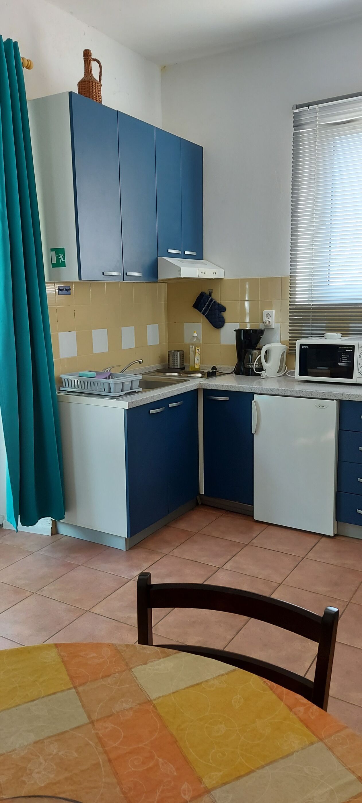 A compact kitchen with blue cabinets, a microwave, a kettle, and a sink.