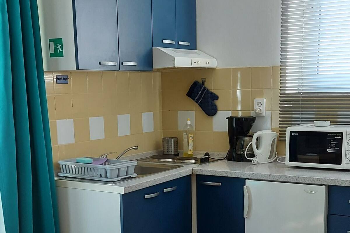 A compact kitchen with blue cabinets, a microwave, a kettle, and a sink.