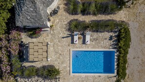 En vy från ovan över ett poolområde med en rektangulär pool, solstolar och en stenbelagd uteplats.