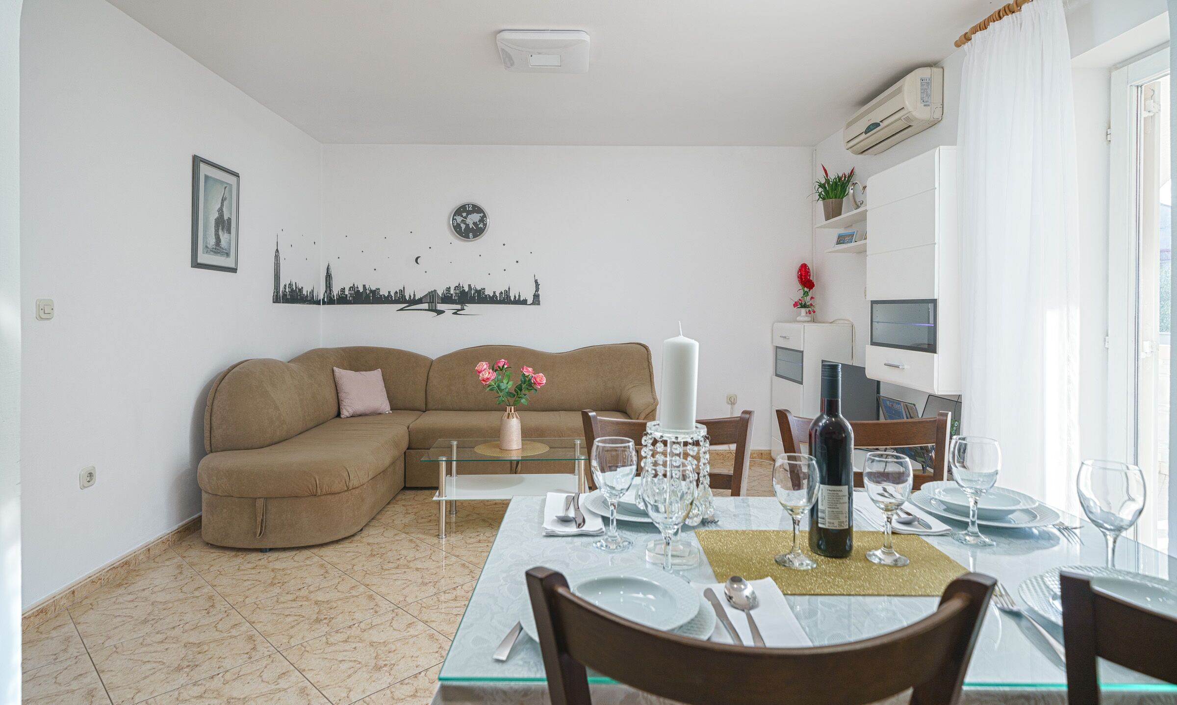 A living room with a brown sofa, a dining table set for four, and a cityscape wall art.