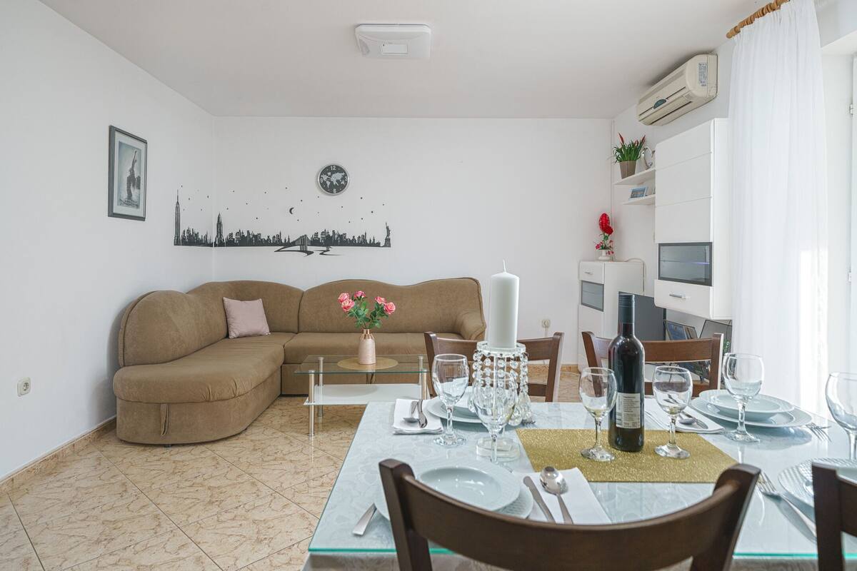 A living room with a brown sofa, a dining table set for four, and a cityscape wall art.