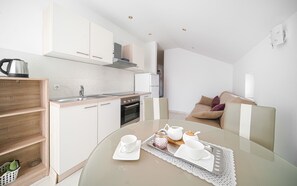 A modern kitchen with white cabinets, a stainless steel kettle, and a dining table set with white cups and a teapot. - Apartments Tamaris (Vodice)