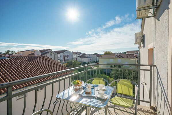 A balcony with a table set for breakfast, overlooking a residential area with houses and a clear sky. - Apartments Tamaris (Vodice)