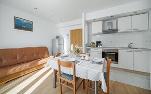 A modern kitchen with white cabinets, a built-in oven, and a dining area with a table set for two. - Apartments Tamaris (Vodice)