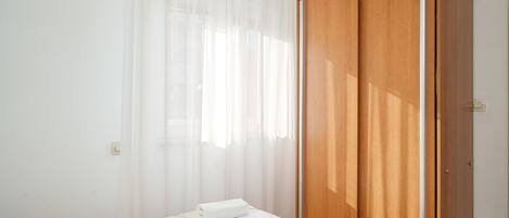A bedroom with a bed, a wooden wardrobe, and sheer curtains.