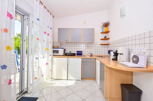 A modern kitchen with white cabinets, a microwave, a coffee maker, and a trash bin. - Apartments Rote Rosen (Sabunike)