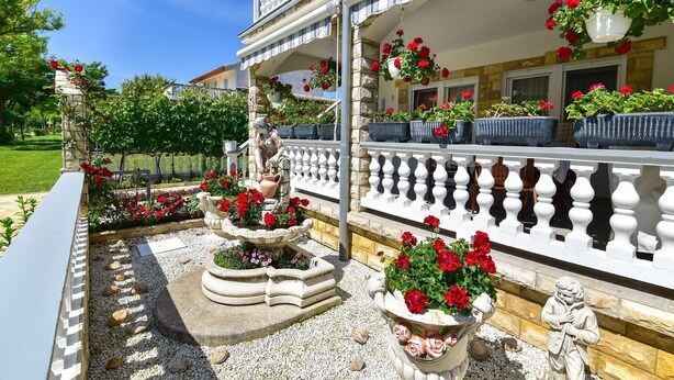 A building with a white balcony, potted plants, and a statue. - Apartments Rote Rosen (Sabunike)