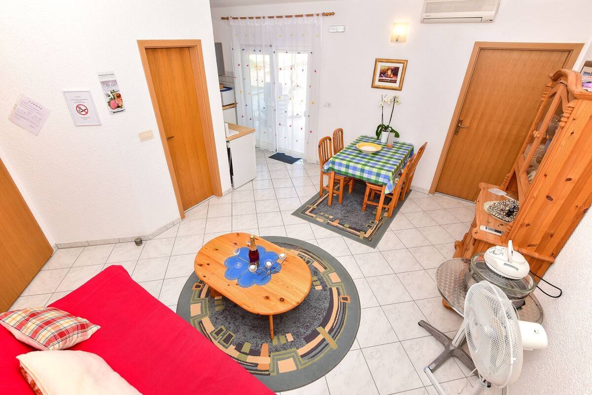 Un espacio habitable compacto con comedor, un sofá rojo, una mesa de madera, un ventilador y una pequeña cocina.