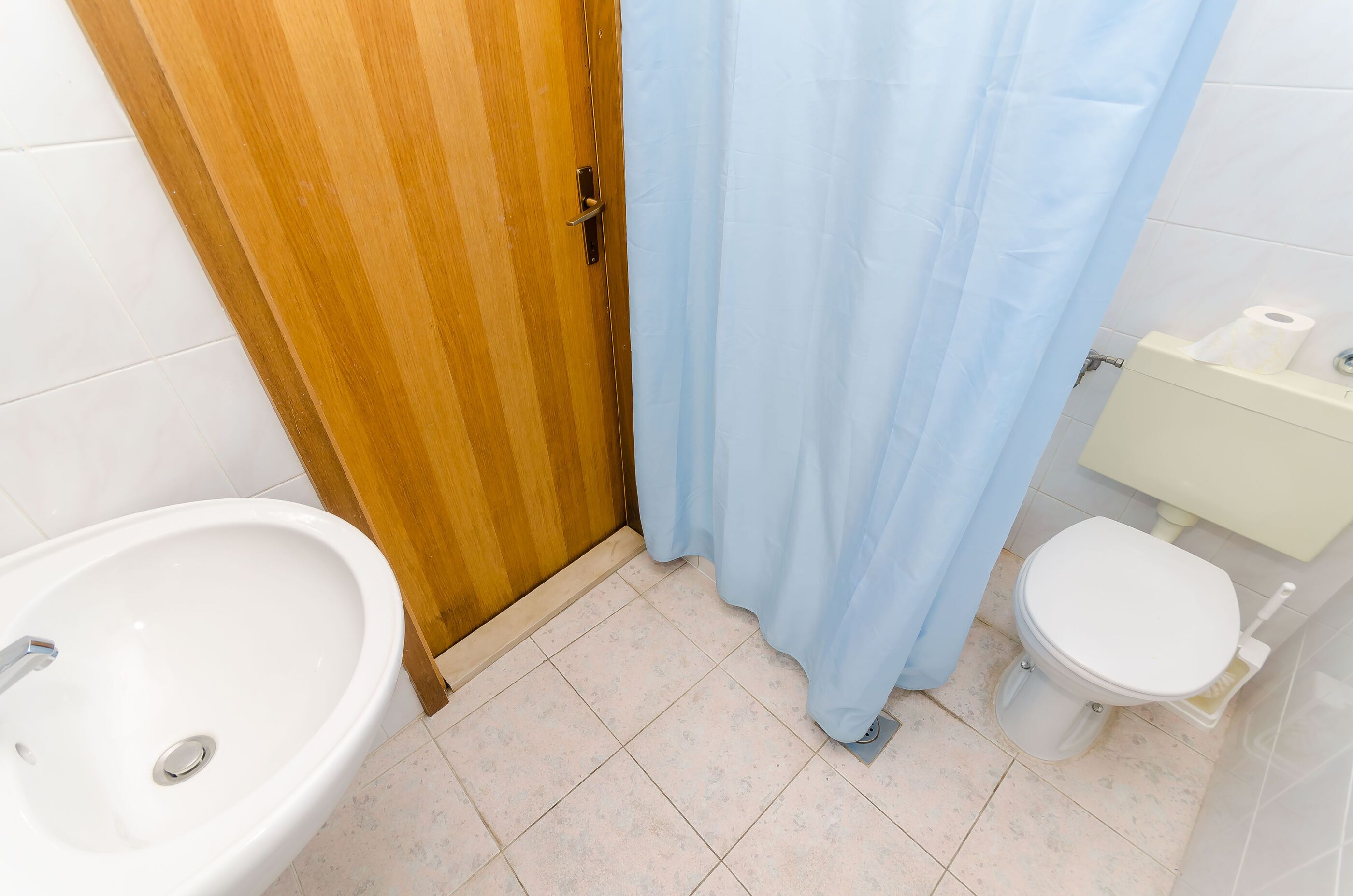 Une salle de bain avec une porte en bois, un lavabo blanc, des toilettes et un rideau de douche bleu.