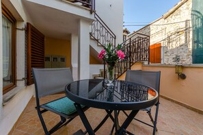 A round glass table with metal chairs, a potted plant, and a staircase leading to an upper floor. - Apartments Old Town (Trogir)