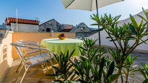 A terrace with a table and chairs, a bowl of fruit, and a large umbrella. - Apartments Old Town (Trogir)